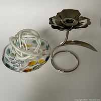 Image showing a multicolored glass paperweight with floral patterns and a white swirl next to a silver-tone metal candle holder with a flower-shaped top and circular base.