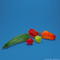 Murano glass zucchini with four ceramic fruit pieces (two peppers, small tomato, bell pepper) on a blue surface.