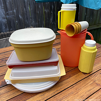 Outdoor photo showing stacked vintage Tupperware including various plastic food storage containers, a large pitcher, small cups, and a thermos-style container.