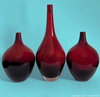 Three ruby red glass vases from IKEA Salong collection shown against a blue background, front view.