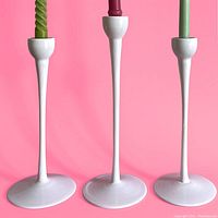 Three white glass candlestick holders on a pink background, showing front view with candles in place showing scale and use.