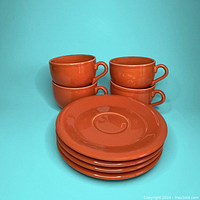Four orange ceramic teacups stacked in two columns, with four orange saucers stacked in front of them.