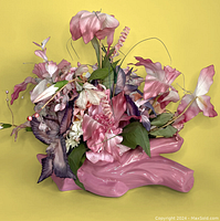 Front angle showing arrangement of various pastel pink and violet silk flowers with green leaves set in pink glossy ceramic log-shaped base.