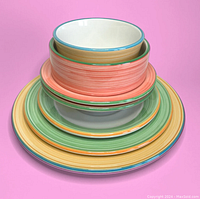 Stack of seven colorful plates and bowls with striped rims in yellow, green, coral, showing size and design.