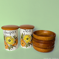 Two ceramic jars labeled Sugar and Tea with hand-painted floral motifs and wooden lids, alongside four teak wooden bowls stacked