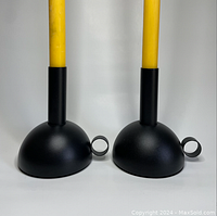 Two black IKEA metal candle holders each holding a yellow candle, shown side by side.
