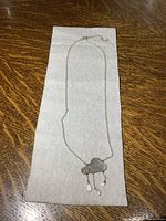 Full view of the silver chain with cloud pendant laid flat on a surface.