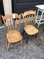 Pair of antique arrow back chairs in solid wood with aged patina and wear, one chair's bottom painted black.