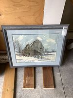 Framed rustic barn print resting on wood surface against plywood background showing the overall artwork and frame