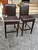 Front and side angle of both wood framed bar height chairs with brown vinyl cushions showing overall condition and design.
