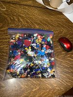 Full ziplock bag filled with assorted building block figures and accessories on a wooden surface, showing a large quantity of items inside.