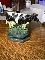 Front and side view of the vintage cast iron door stop featuring a black and white spotted cow on a green base with textured grass detail.