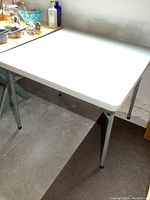 Side view of the white resin plastic top and grey folding metal legs of the table.