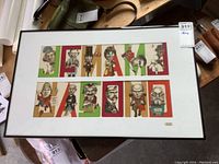 Full view of the framed calendar art spelling 'CANADA' with caricatures inside each letter, colors red, green, and tan, on a white mat in a thin dark frame.