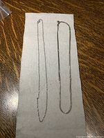 Two chains laid out flat on white cloth: left chain is thin white gold chain, right chain is thicker sterling silver chain.