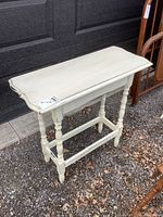 Front angle view showing white painted turned legs and slightly curved table top edges with distressing.