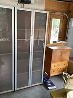 Front view of beige IKEA enclosed bookcase with two frosted glass doors and wood-finish sides, positioned next to wood furniture.