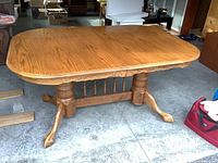 Angled side view of the oak dining table showing the top and double pedestal base with carved details and claw feet.