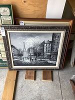 Framed oil painting on canvas showing a Paris street scene with the Eiffel Tower in the distance, displayed upright with visible ornate frame details.