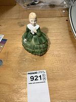 Front view of the Royal Doulton Belle porcelain figurine on wooden surface with measurement card showing lot number 921