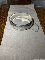 Photo of the front and side of a wide sterling silver bangle bracelet showing floral engravings and attached safety chain.