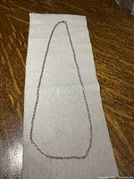 Full view of the sterling silver double intertwined chain necklace laid flat on a neutral surface.