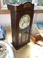 Front and side view of vintage Divina wall clock showing wooden case, decorative top, and glass panel at bottom