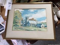 Framed watercolour painting showing church with spire and surrounding landscape under blue sky.