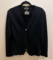 Front view of black knit cardigan with gold buttons hanging on a hanger.