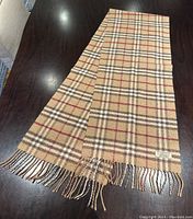 Full view of scarf laid flat on dark wood surface showing check pattern, fringed ends and overall condition