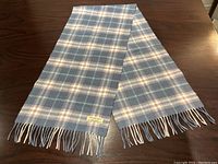 Full-length view of scarf laid flat on wooden surface, showing tartan pattern and fringe ends