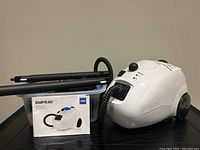 Steam cleaner unit with hose, extension wands, instruction manual and storage tub on table