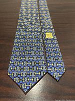 Full-length view of tie laid flat on wooden surface, showing overall blue background and gold bit pattern