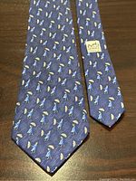 Full view of the Hermes silk tie showing the repeating pattern of men with yellow umbrellas on blue background and the overall condition.