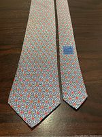 Full view of the Hermes silk tie showing the repeating geometric ring pattern in blue, red, white, and black on a ribbed silk fabric.