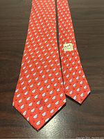 Full view of Hermes red silk tie with frog pattern and Hermes Paris label sewn on the back side.