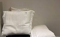 Two large white quilted sham pillows stacked on a surface next to a quilt folded on the right.