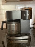 Front view of Keurig coffee maker with glass carafe on black countertop, showing overall condition and design.