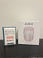 Both the book and the LED light therapy mask's original boxed packaging placed side by side on a table surface, showing front covers clearly.