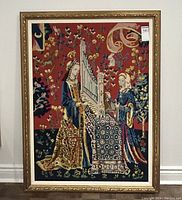 Full frontal view of the vintage medieval scene needlepoint embroidery in a gold decorative frame hanging on a white wall.