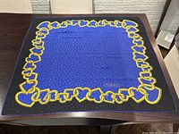 Full view of Tiffany & Co. silk scarf laid flat showing blue center with repeating T pattern, gold heart-linked chain border and black outer border.