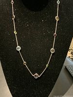 Front view of sterling silver station necklace displayed on black stand showing multiple colorful gemstones spaced along chain.