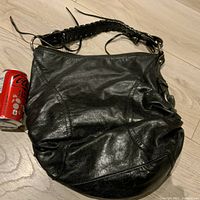 Full view of the black leather bag showing overall shape and braided shoulder strap next to soda can for scale.