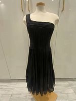 Front view of the black silk one-shoulder dress on a mannequin, displaying the delicately ruched bodice and flared skirt detail.