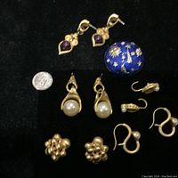 All jewelry pieces laid out on black surface including earrings and brooch with a quarter for size reference.
