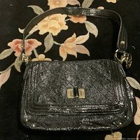 Front view of the black patent leather shoulder bag displaying texture and twist-lock clasp.