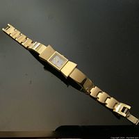 Full view of the goldtone bow-shaped watch with linked bracelet strap laid flat on black reflective surface.