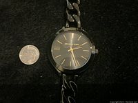 Michael Kors watch face, round black dial with gold markers, hand positions show about 10:07:27, black chain link band visible