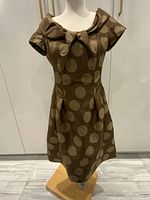 Front view of the brown polka dot dress on a mannequin showing the large bow detail on the neckline.