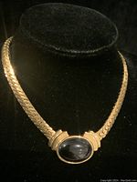 Full view of the gold tone Napier necklace with black cabochon on black display stand.